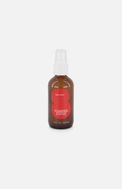 A brown glass spray bottle with a white cap and red FLAMINGO ESTATE label, labeled Roma Heirloom Tomato Room Spray, is displayed on a white background. This room spray captures the fresh scent of a summer garden.