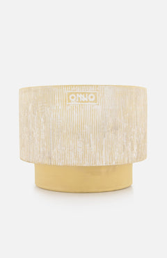 The Capri L Sao Tome Candle by ONNO is a round, textured beige and gold planter with vertical white lines and a small ONNO logo on the front, evoking designer elegance against a plain white background.