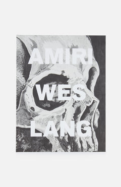 A grayscale human skull illustration features bold white "AMIRI WES LANG" text, showcasing the AMIRI Wes Lang x RIZZOLI collaboration, with the artist’s signature at bottom left in tribute to AMIRI Autumn-Winter 2022.