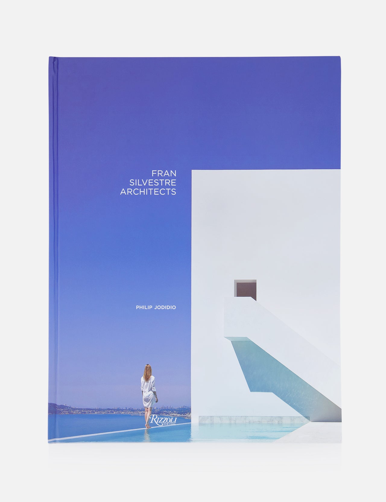 The book "Fran Silvestre Architects" by RIZZOLI features a cover with minimalist architecture—a sleek white building, blue stairs, a woman by the pool, and a clear sky—ideal for fans of luxury interior design.