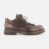 The OFFICINE CREATIVE Artik Flex Lace Low Boot is displayed in side profile on a white background, showcasing its brown leather construction, black laces threaded through metal eyelets, and a thick, rugged rubber sole—expertly handcrafted in Italy.