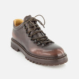 The OFFICINE CREATIVE Artik Flex Lace Low Boot—a single brown leather hiking shoe featuring black laces, metal eyelets, and a thick, rugged sole inspired by vintage lace-up boots—displayed against a white background.