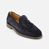 The Opera Flexi Tassel Loafer by OFFICINE CREATIVE is crafted from Italian navy blue suede and showcases refined tassels on the vamp, a rounded toe, light brown inner lining, and a flat brown sole, all elegantly presented against a white background.
