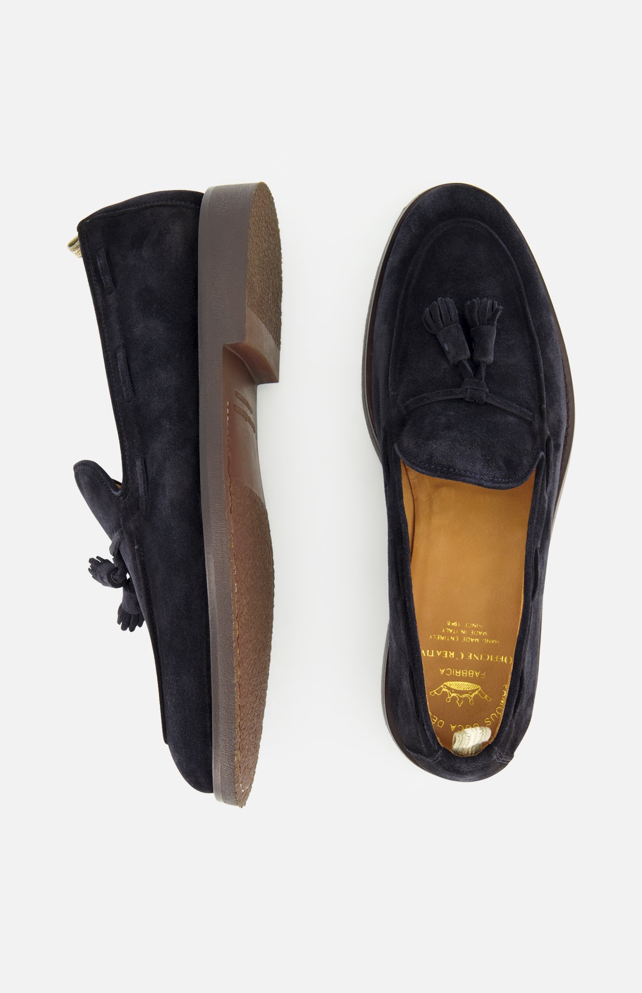A pair of Opera Flexi Tassel Loafers by OFFICINE CREATIVE, crafted in classic Italian style with black suede uppers—one shown from the side and one from above—featuring brown soles, tan leather insoles adorned with gold brand lettering, and elegant tassel details.