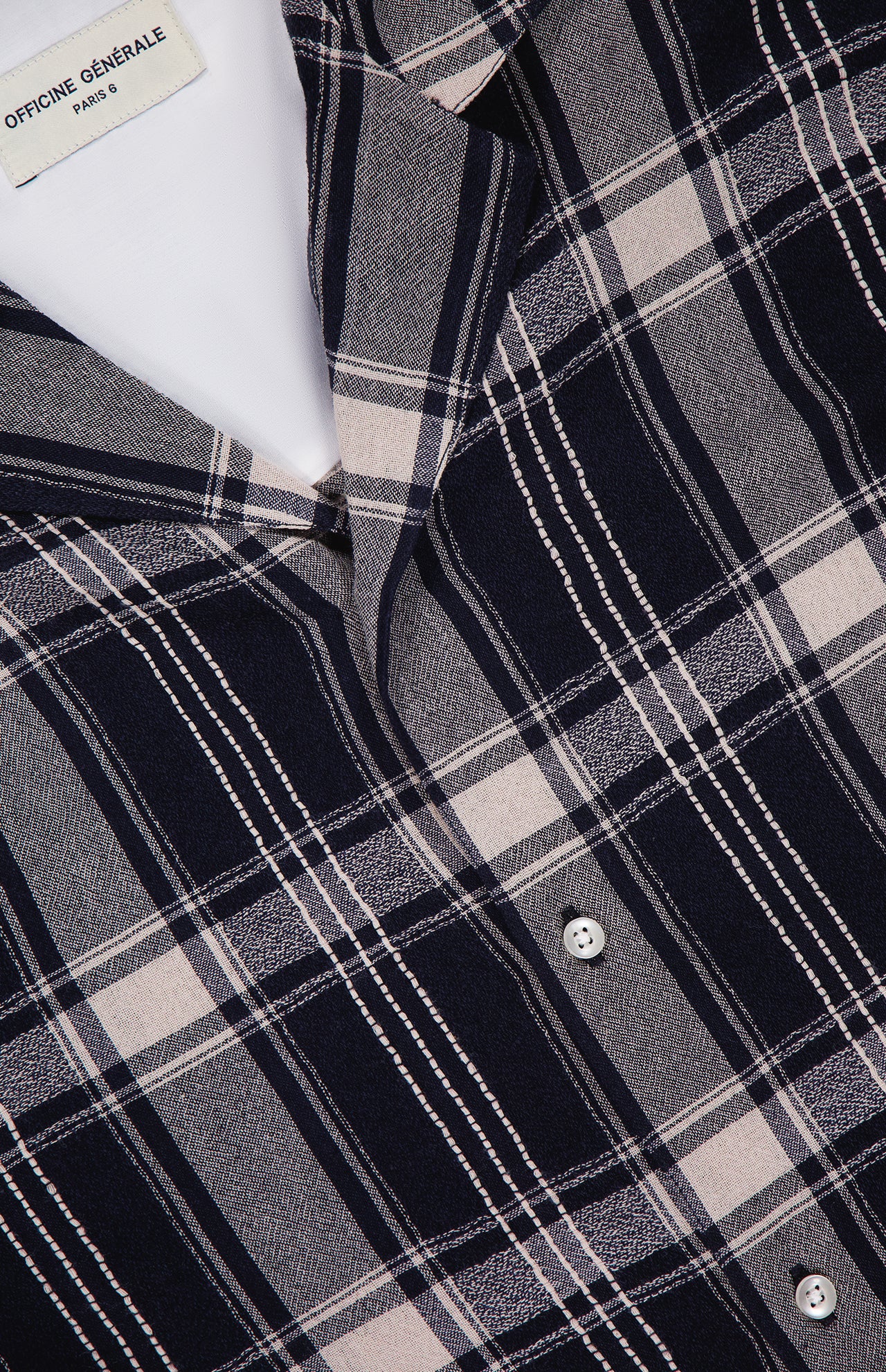 Close-up of the Eren Long Sleeve Gaze Checkered Shirt by OFFICINE GÉNÉRALE, featuring a navy blue, gray, and white plaid pattern with white buttons and a visible OFFICINE GÉNÉRALE PARIS label. Expertly crafted in Portugal, this classic long-sleeved shirt highlights exceptional attention to detail and timeless style.