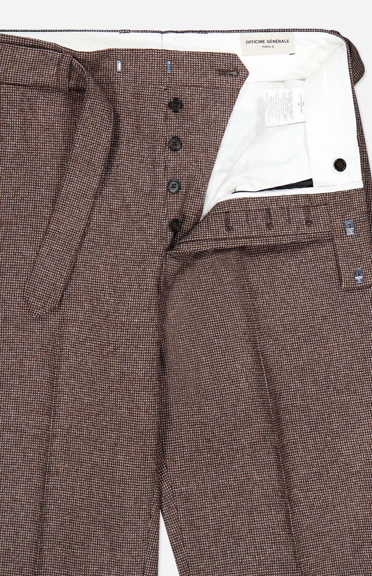 OFFICINE GÉNÉRALE Hoche Wool Trouser Pants in brown plaid, featuring a removable belt, button fly, and a white inner waistband lining. The light brown trousers are partially unbuttoned and laid flat to reveal the interior labels and stitched details.