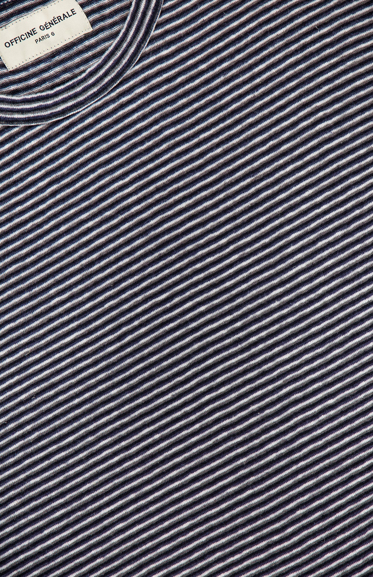 Close-up of the OFFICINE GÉNÉRALE Multico Long Sleeve Stripe T-shirt in navy and white, featuring a striped cotton-linen fabric with thin, evenly spaced lines and a visible brand label at the collar. This t-shirt offers a Parisian-inspired fit for an effortlessly stylish look.
