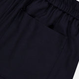 A close-up of the OFFICINE GÉNÉRALE Nelson Twill Trouser Pants in dark navy highlights the elastic waistband and a single square pocket stitched onto the smooth, slightly shiny virgin wool twill fabric.