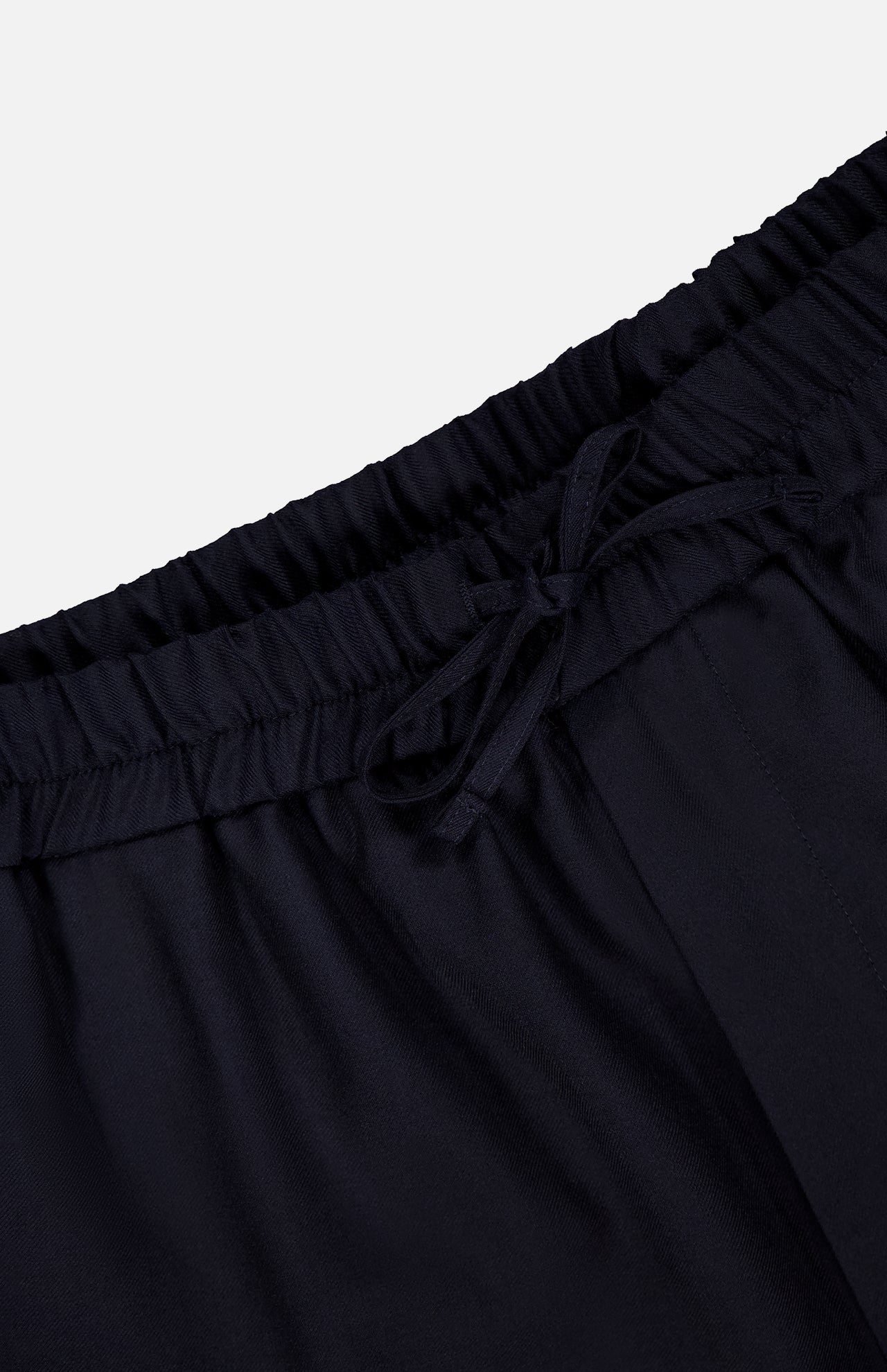 Close-up of the waistband of the OFFICINE GÉNÉRALE Nelson Twill Trouser Pants in dark navy, featuring a drawstring tie, gathered elastic material, and part of the upper pant legs set against a plain light background.
