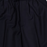 Close-up of the Nelson Twill Trouser Pants by OFFICINE GÉNÉRALE in dark navy. These pants feature an elastic waistband with a drawstring, crafted from smooth, slightly shiny virgin wool twill. The relaxed, wide-leg silhouette is designed with minimal detailing for a clean finish.