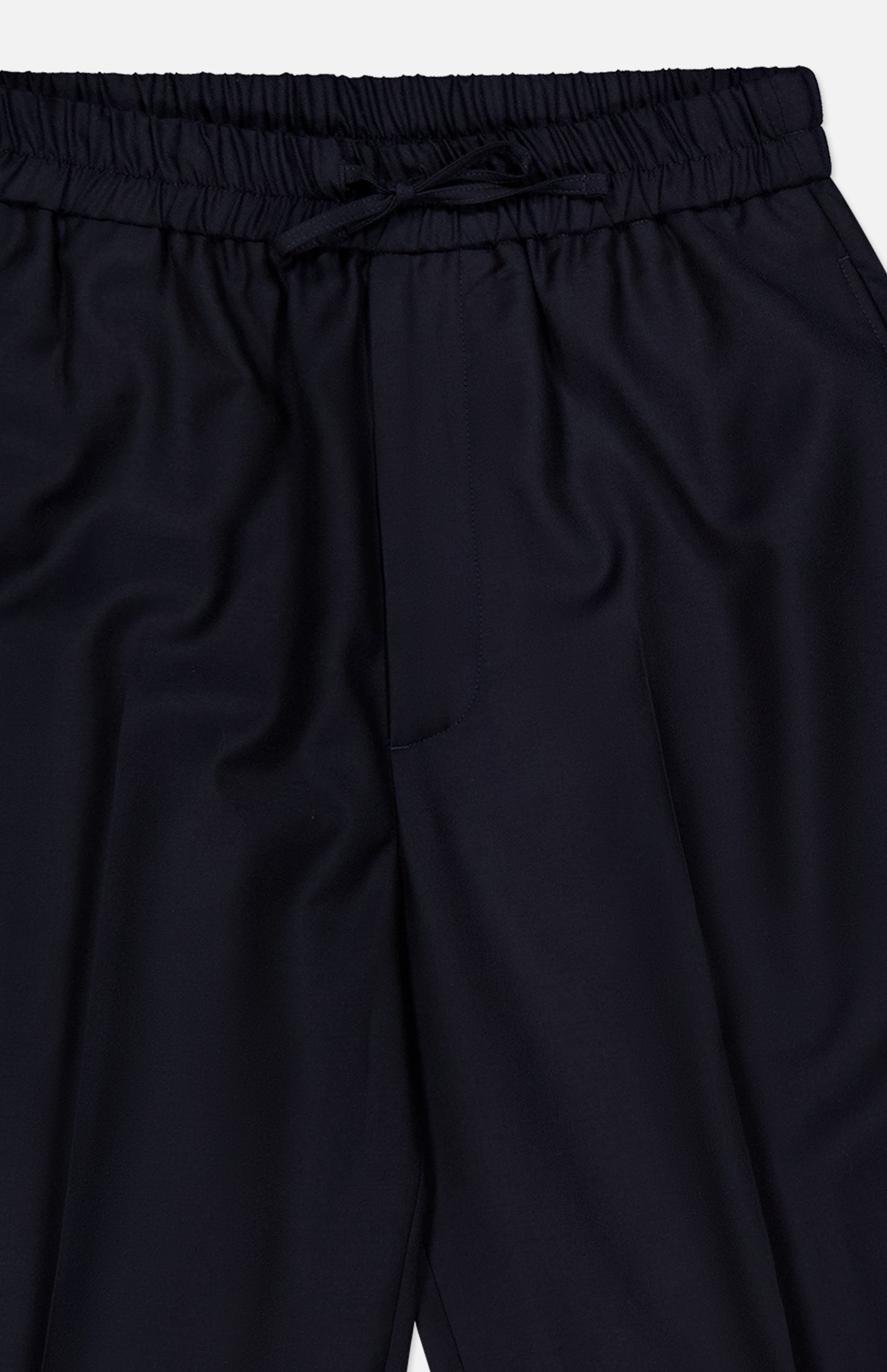 Close-up of the Nelson Twill Trouser Pants by OFFICINE GÉNÉRALE in dark navy. These pants feature an elastic waistband with a drawstring, crafted from smooth, slightly shiny virgin wool twill. The relaxed, wide-leg silhouette is designed with minimal detailing for a clean finish.