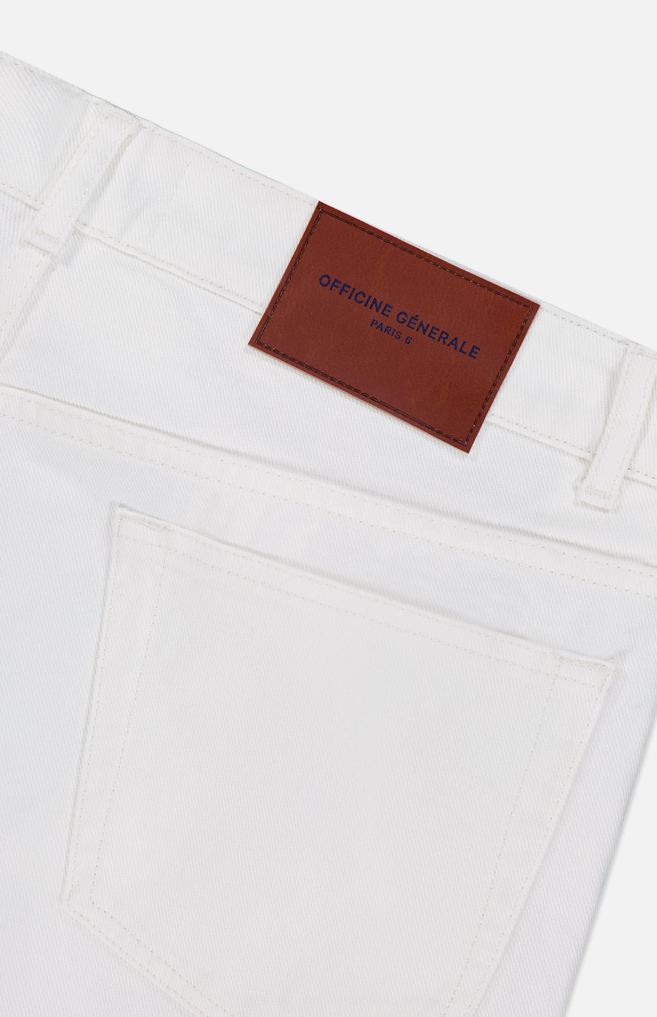 Close-up of the back pocket and waistband of OFFICINE GÉNÉRALE Vintage Original Wash Denim Pants, featuring a brown leather brand patch, visible belt loops, subtle stitching, and classic 5-pocket design.