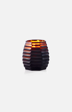 The ONNO Amber Cubo S Ginger Fig Candle glows in a dark, ribbed glass holder with a honeycomb pattern, filling the space with fig and ginger fragrance against a plain white background.