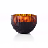 The ONNO Amber Ellipse L Ginger Fig Candle is shown against a white background. Its round, amber glass bowl features a ribbed texture and glows warmly inside, highlighting the candle's translucent quality and inviting ambiance.
