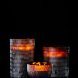 Three ONNO Amber Rhombus L Ginger Fig candle holders glow warmly against a black background. Two tall holders flank a smaller round one, creating a designer ambiance with luxury fragrance for your home.