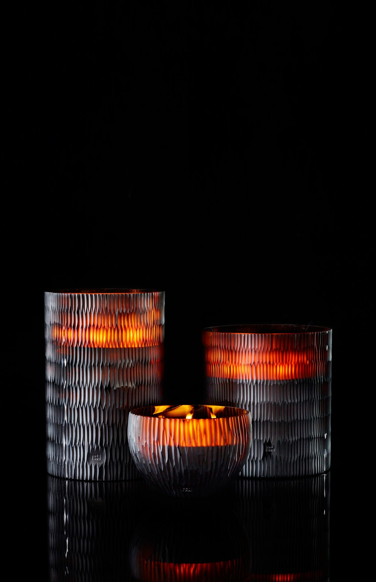 The ONNO Amber Rhombus L Sage Candle glows warmly in a textured glass holder, set against a black background, showcasing hand-poured craftsmanship and adding designer fragrance to your space.