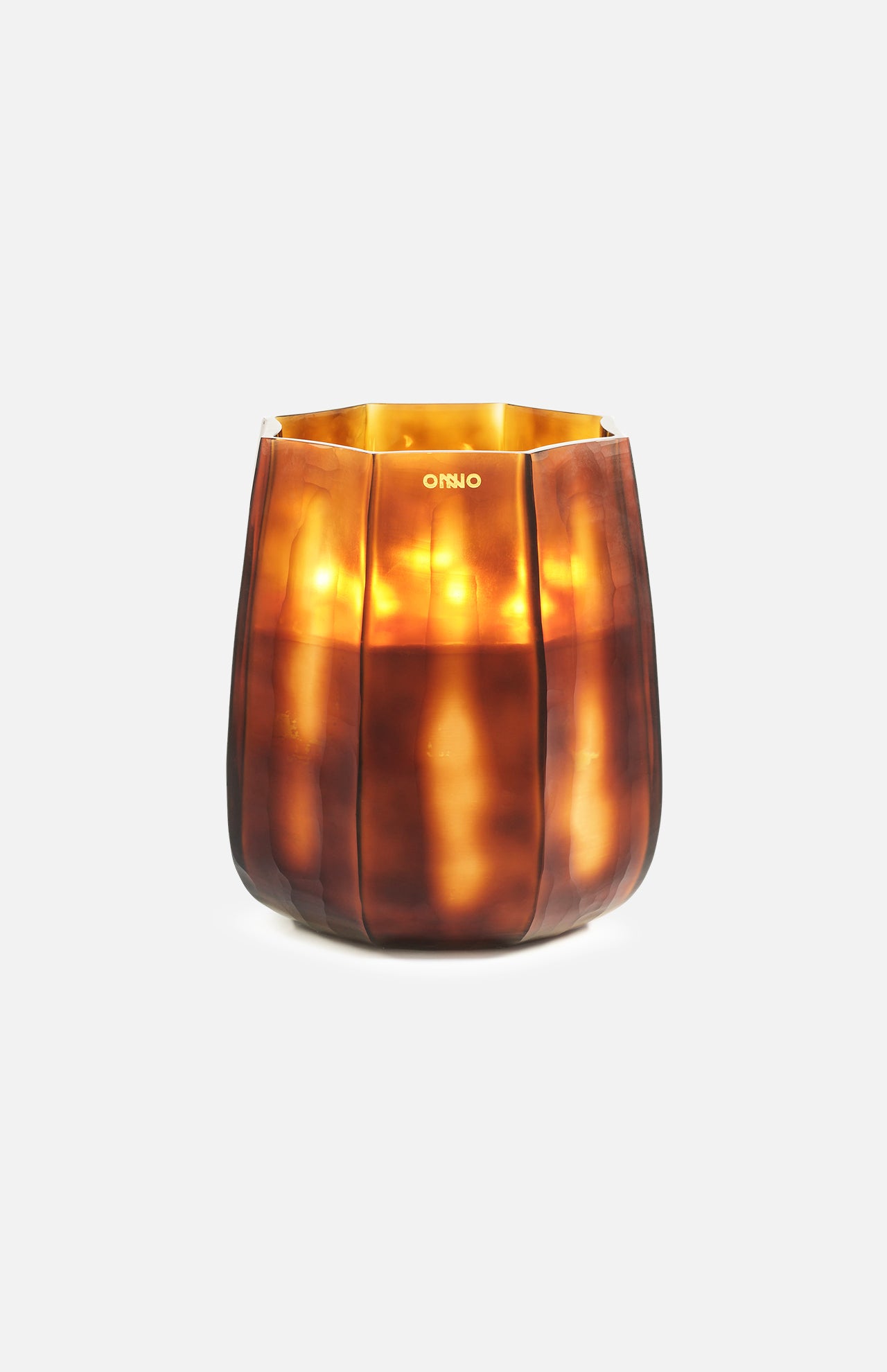 The ONNO Embrace L Sage Candle, set in a brown faceted glass holder with vertical ridges and a tapered shape, emits a warm golden glow—perfect as luxury designer decor against a plain white background.