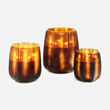 Three ONNO Embrace S Sage candle holders in brown and gold glass are shown against a white background. Each features a glossy, translucent finish and gives off a warm amber glow—ideal for displaying a luxury scented candle.