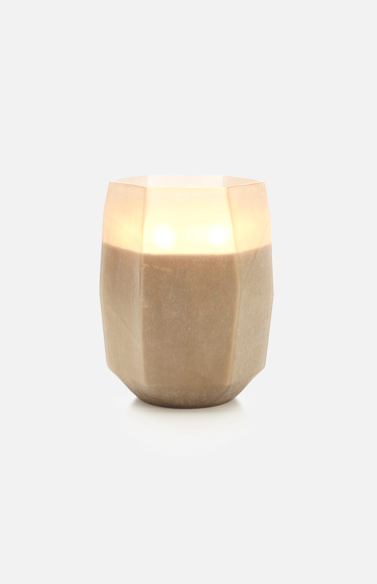 The ONNO Terre Light Smoked XL Zanzibar Candle glows warmly inside a beige, faceted holder, illuminating against a plain white background.