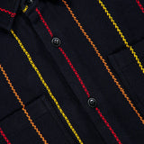 Close-up of the Pinstripe Roundtail Overshirt by ORIGINAL MADRAS, crafted from dark Indian cotton with vertical red, orange, and yellow stitched pinstripes, featuring black buttons, two chest pockets, and a yellow label inside the collar.