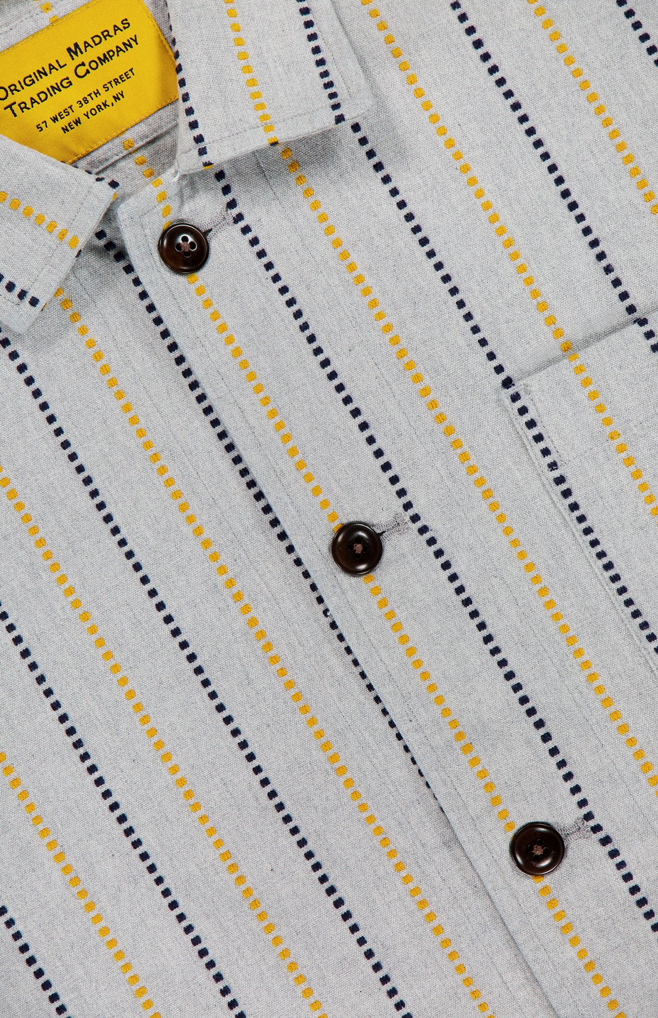 Close-up of the Stripe Jacquard Shirt Jacket by ORIGINAL MADRAS, featuring soft Indian cotton in light gray with vertical yellow and navy dotted stripes, dark buttons, and a yellow brand label sewn inside the collar.