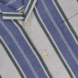 Close-up of the ORIGINAL MADRAS Stripe Lax Camp Shirt made from pure Indian cotton with vertical blue, green, and white stripes, beige buttons, and a yellow neck tag reading Original Made Trading Company. Fabric has a textured look.