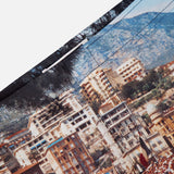 Close-up of ORLEBAR BROWN’s Bulldog Photographic Race Car Shorts, showcasing a detailed coastal Grand Prix scene with colorful buildings, flags, people, and mountains. Visible stitching adds texture—ideal for stylish swimwear.