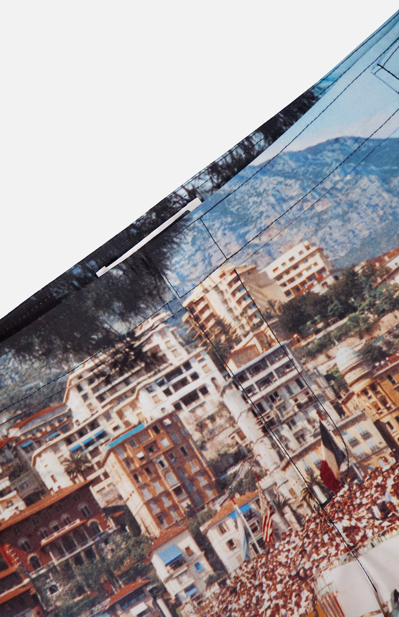 Close-up of ORLEBAR BROWN’s Bulldog Photographic Race Car Shorts, showcasing a detailed coastal Grand Prix scene with colorful buildings, flags, people, and mountains. Visible stitching adds texture—ideal for stylish swimwear.