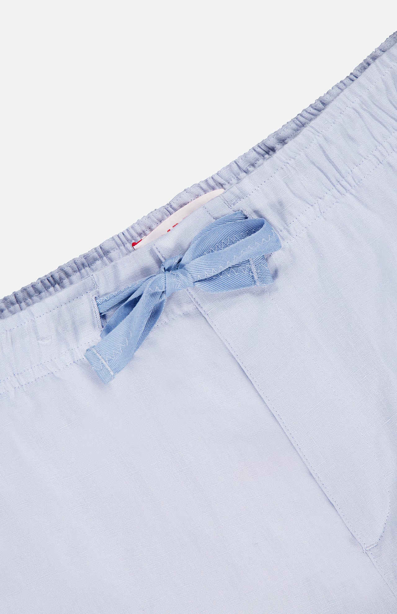 Close-up of the waistband of ORLEBAR BROWN's Alex Relaxed Linen Pants in light blue, featuring an elastic band and a matching fabric bow at the center front. The soft linen material looks lightweight and comfortable.