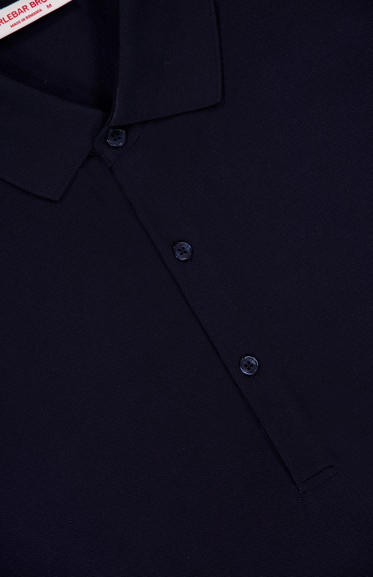 Close-up of the ORLEBAR BROWN Bruno 3 Button Pique Polo Shirt in dark navy, showing its classic fit, textured cotton pique fabric, collar, three-button front placket, and a visible clothing label at the top left.