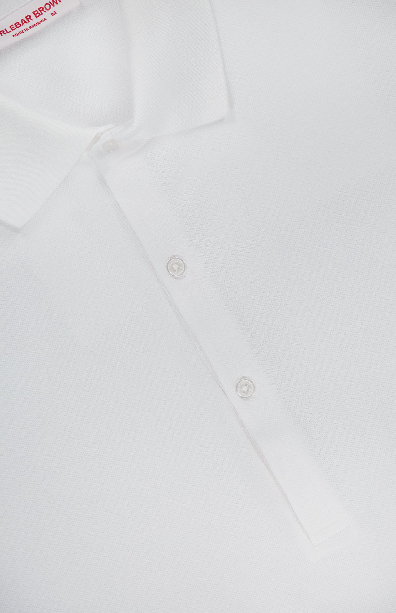 Close-up of the ORLEBAR BROWN Bruno 3 Button Pique Polo Shirt in classic fit white cotton pique, showcasing three white buttons on the placket and a partially visible red and white label at the neckline.
