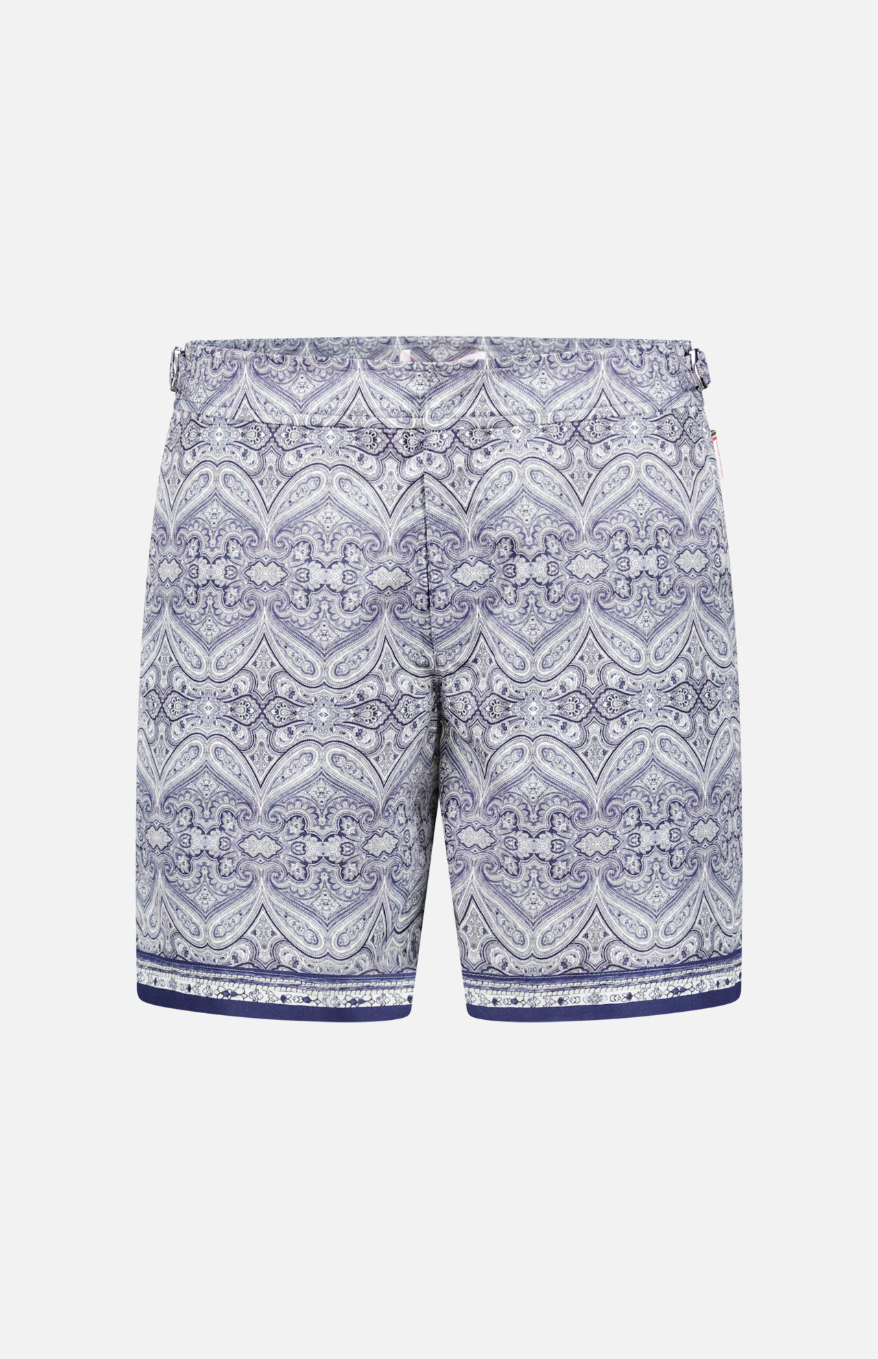 The ORLEBAR BROWN Bulldog Carnival Swim Trunk features a blue and white paisley print, elastic waistband, adjustable side buckles, and dark blue stripes at the bottom, displayed on a plain white background.