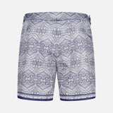 The ORLEBAR BROWN Bulldog Carnival Swim Trunk features a detailed blue and white paisley print, adjustable side buckles, and a dark blue hem stripe, shown against a plain white background.