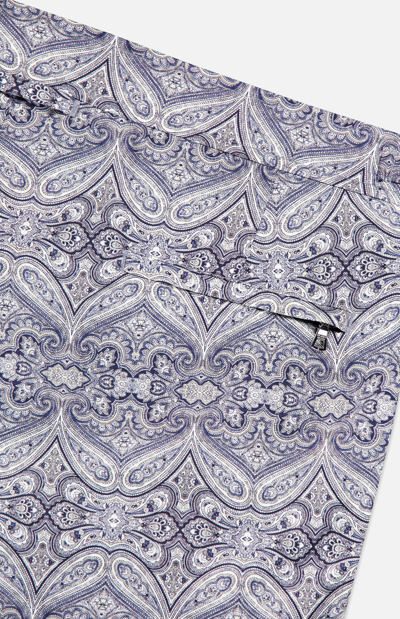 The ORLEBAR BROWN Bulldog Carnival Swim Trunk features a detailed paisley print in blue and gray, complete with a small horizontal zippered pocket.