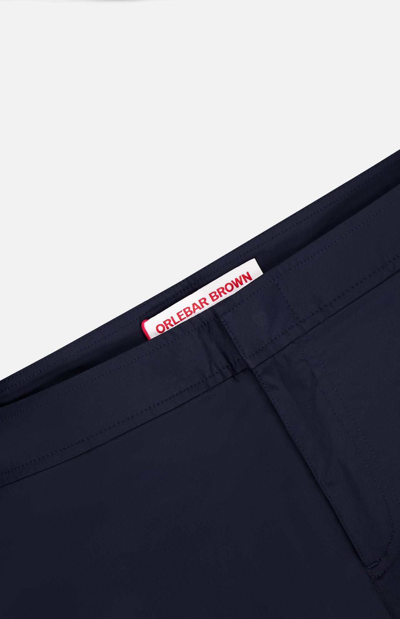 Close-up of Bulldog Stretch Shorts by ORLEBAR BROWN, showing a white inner waistband label with red branding and adjustable side tabs, set against a plain light background.
