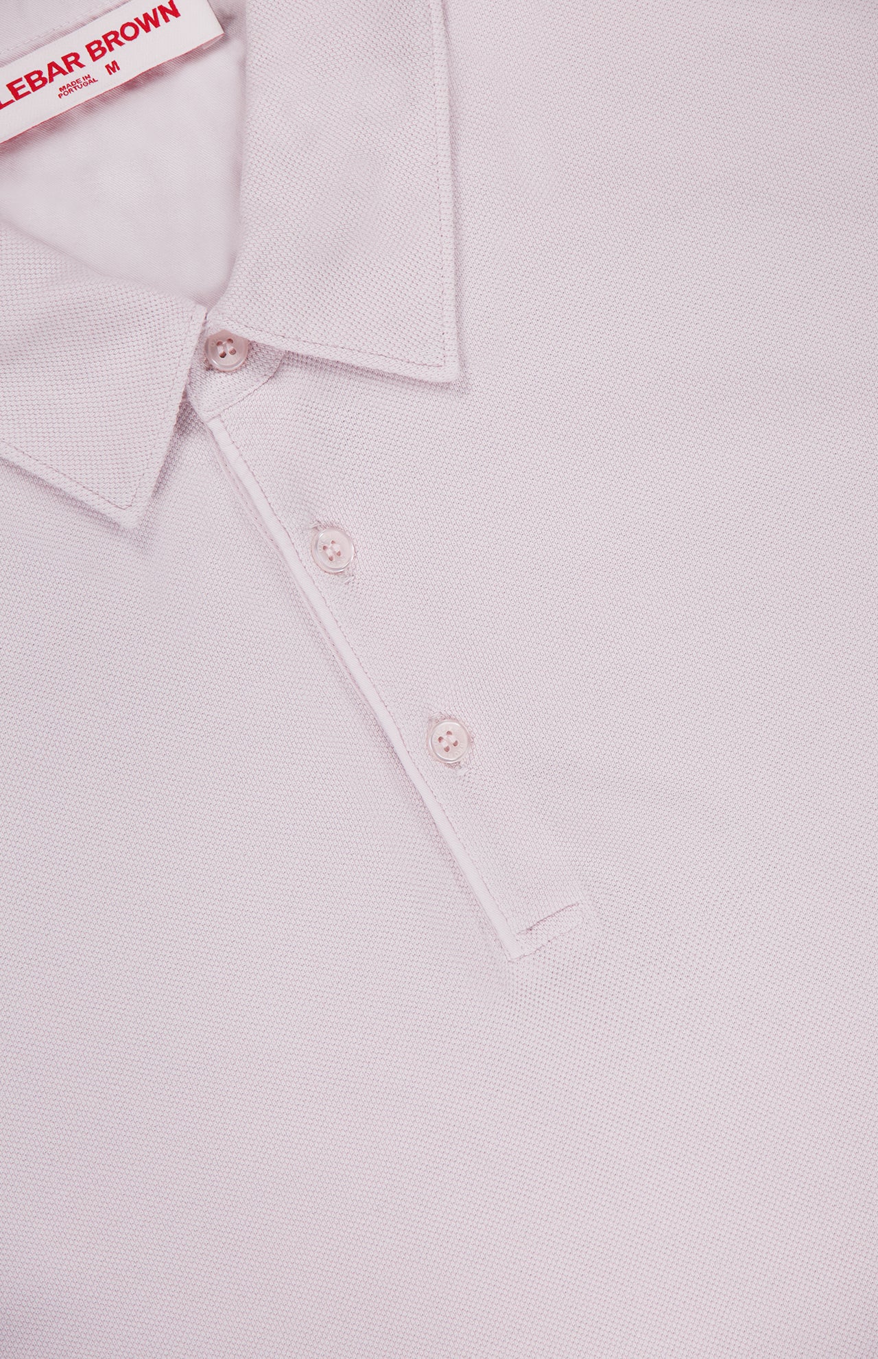 A close-up of a light pink Garfield Long Sleeve Polo Shirt by ORLEBAR BROWN, made from cotton pique jersey with a collar, three buttons, and a red and white brand label inside the collar.