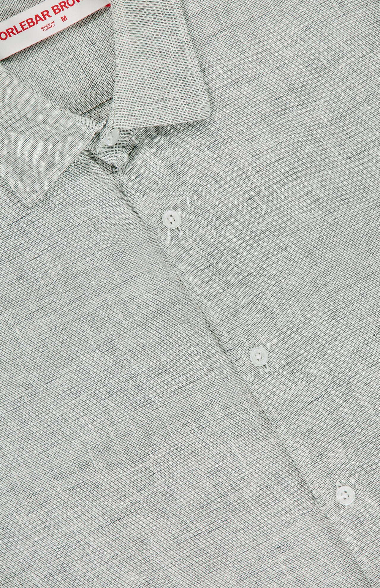 A close-up of the ORLEBAR BROWN Giles Linen II Shirt in light grey, featuring white buttons, a visible collar, woven patterned lightweight linen fabric, and a partially visible clothing label—ideal for a stylish summer look.