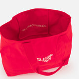 The Beach Bound Bag by ORLEBAR BROWN is a bright red organic cotton canvas tote with the brand name printed outside. Inside, a pocket features "FULL BEACH AHEAD" in white. The bag has two handles and comes empty.