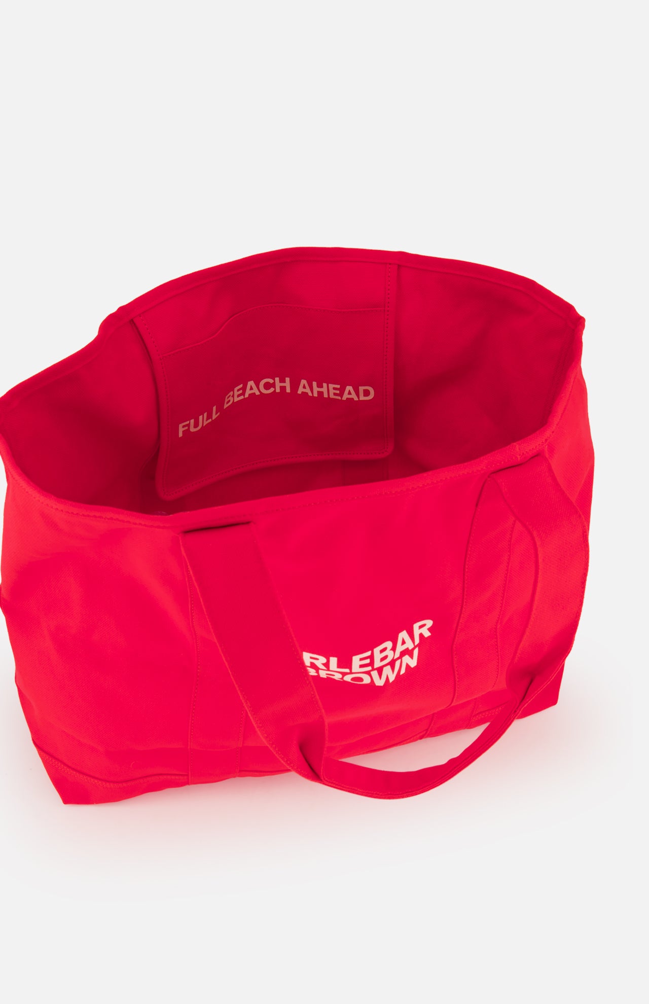 The Beach Bound Bag by ORLEBAR BROWN is a bright red organic cotton canvas tote with the brand name printed outside. Inside, a pocket features "FULL BEACH AHEAD" in white. The bag has two handles and comes empty.