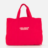 The Beach Bound Bag by ORLEBAR BROWN is a bright red organic cotton canvas beach bag with two handles and "ORLEBAR BROWN" in white centered on the front, shown against a plain white background.