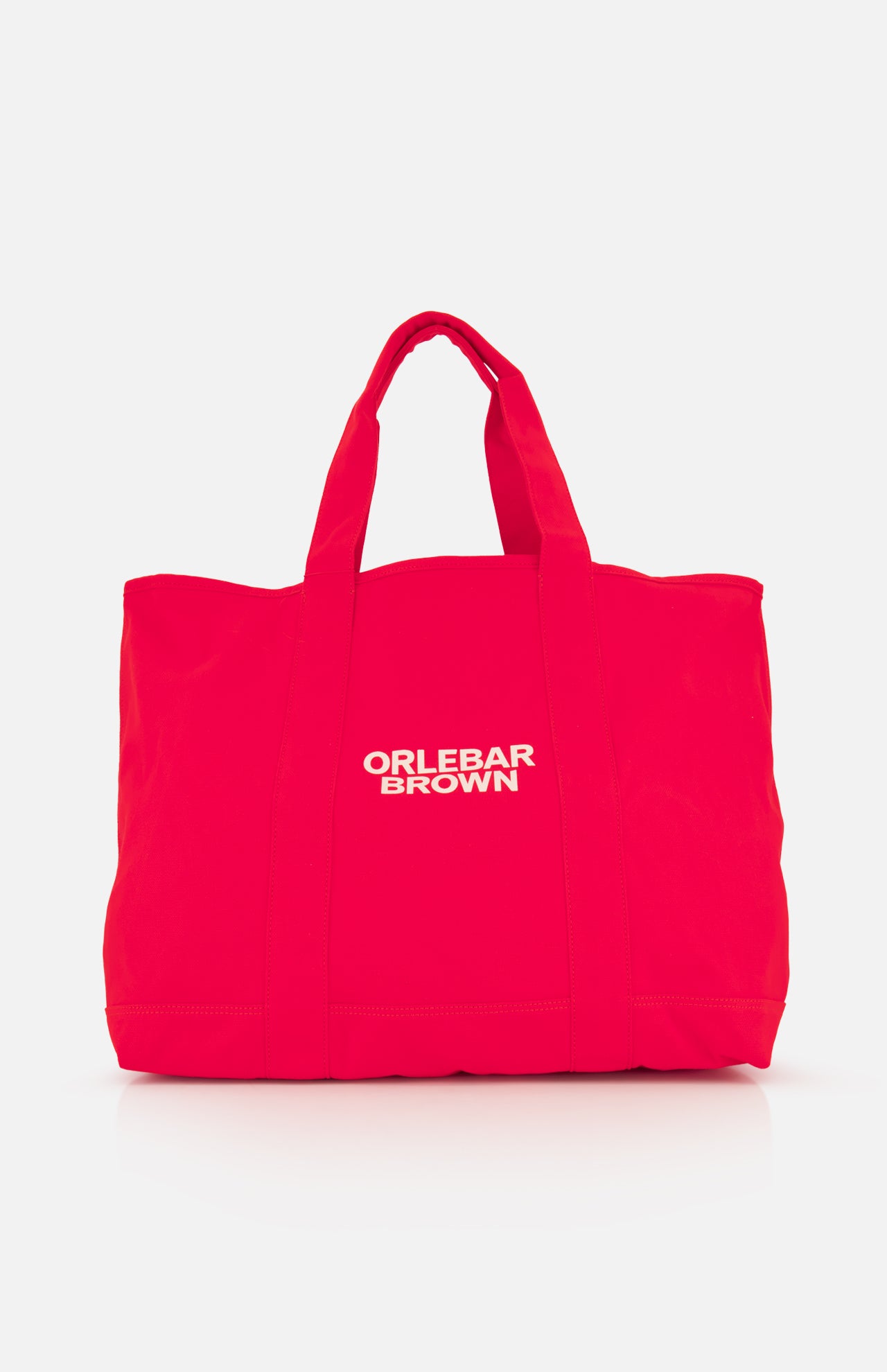 The Beach Bound Bag by ORLEBAR BROWN is a bright red organic cotton canvas beach bag with two handles and "ORLEBAR BROWN" in white centered on the front, shown against a plain white background.