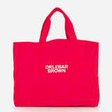 The Beach Bound Bag by ORLEBAR BROWN is a bright red organic cotton canvas tote with two handles and a white centered logo, shown on a plain white background.