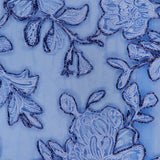 Close-up of the PAMELLA ROLAND Raffia Embellished Gown, showcasing delicate blue floral lace with shimmering embroidery on a sheer light blue background—ideal for special occasions.