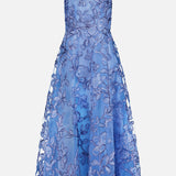 The Raffia Embellished Gown by PAMELLA ROLAND is a sleeveless, cornflower blue dress with a fitted bodice, flared mid-length skirt, intricate floral pattern, and sheer detailing on the upper chest and shoulders.