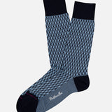 The Vaughan Patterned Sock by PANTHERELLA is a blue dress sock featuring navy diamond-shaped geometric patterns, black heels, toes, and cuffs, plus a small white logo on the sole, shown on a plain white background.