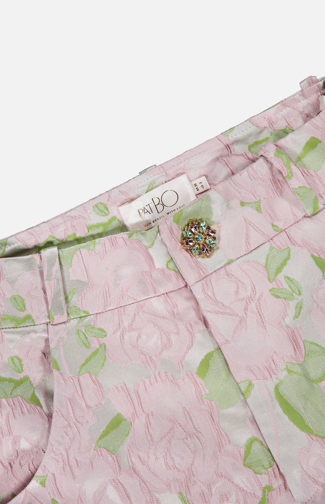 Close-up of PATBO’s Garden Jacquard Pants in pastel pink and green, featuring a jeweled button and signature brand label at the waistband—feminine trousers perfect for a garden party aesthetic.