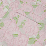 Close-up of fabric from PATBO's Garden Jacquard Pants, showcasing a delicate pink floral pattern with green leaves that evokes a garden party feel. The image highlights a pocket sewn onto the textured, woven material, emphasizing the intricate flower motif and pastel jacquard design.
