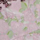 A close-up of the PATBO Garden Jacquard Crystal Top reveals a delicate pink floral jacquard fabric adorned with green leaves and accented by an embellished trim of pink and silver gemstones along the top edge. The textured rose pattern exudes pastel elegance reminiscent of a corset top, while the sparkling crystal details create a striking, statement look ideal for nights out.