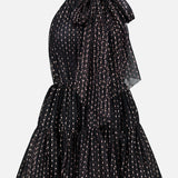 The Olga Tulle Short Dress by PATBO is a black sleeveless mini dress with a halter neckline, highlighted by a statement bow at the neck and a tiered, ruffled skirt. Its tulle fabric features vertical rows of small, light-colored dots for a touch of playful elegance.