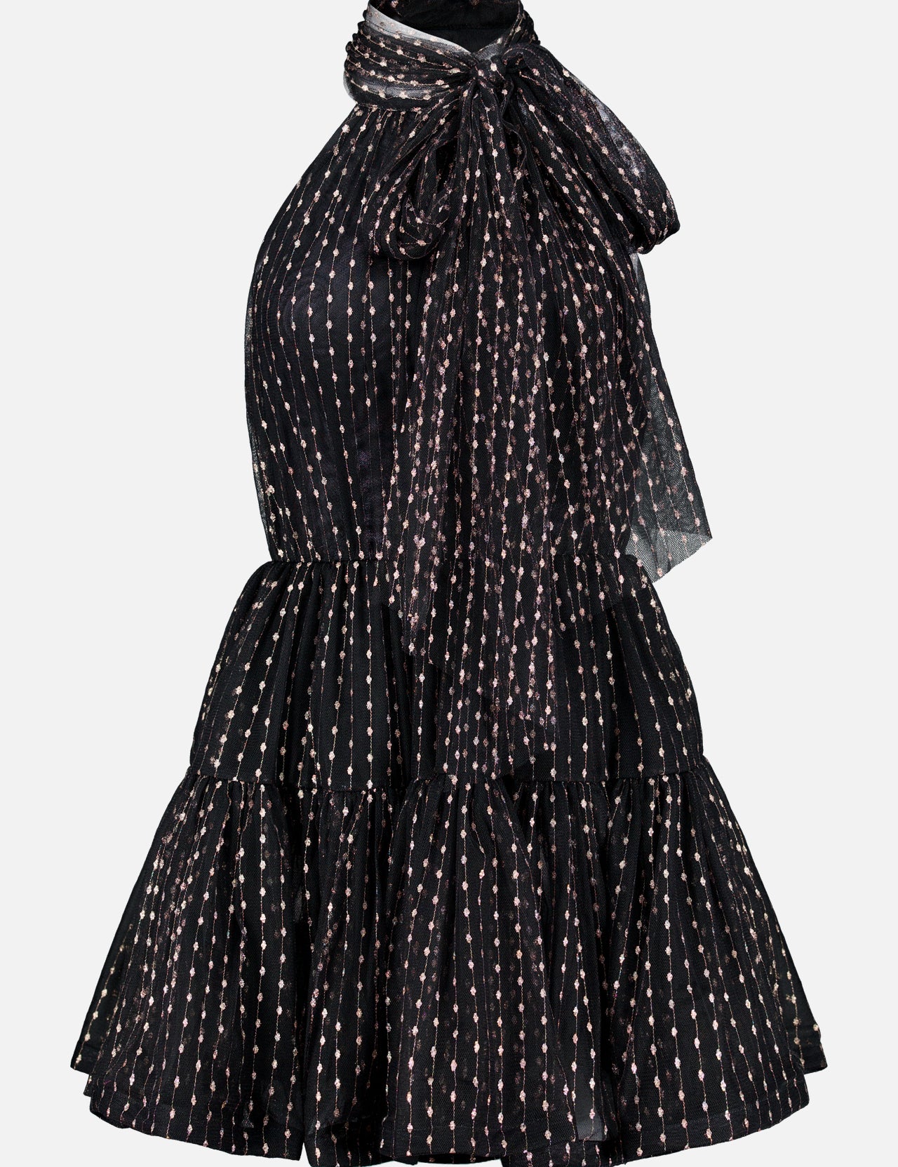 The Olga Tulle Short Dress by PATBO is a black sleeveless mini dress with a halter neckline, highlighted by a statement bow at the neck and a tiered, ruffled skirt. Its tulle fabric features vertical rows of small, light-colored dots for a touch of playful elegance.
